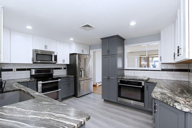 kitchen with dark stone countertops, gray cabinets, and stainless steel appliances