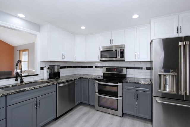 kitchen featuring dark stone counters, gray cabinetry, a sink, appliances with stainless steel finishes, and tasteful backsplash