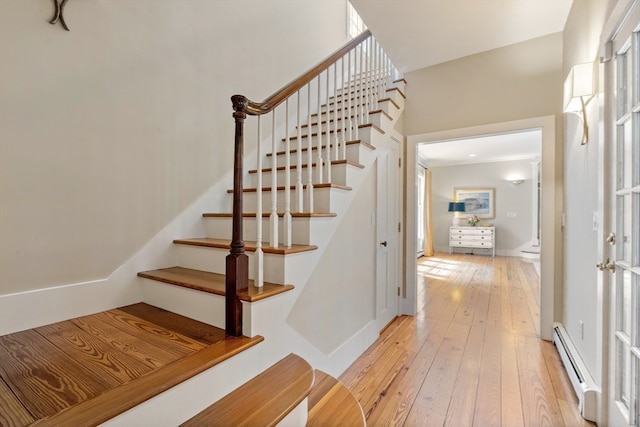 staircase with a baseboard heating unit and wood-type flooring