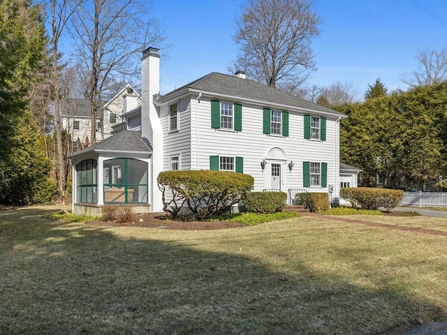 colonial inspired home featuring a chimney, roof with shingles, a front lawn, and a sunroom