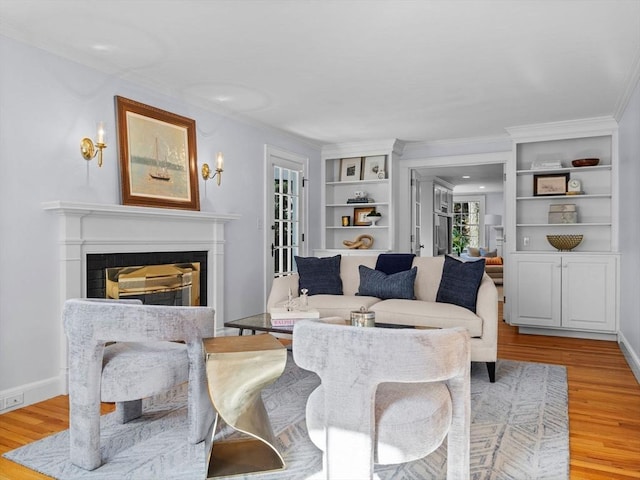 living room with light wood-type flooring, baseboards, a glass covered fireplace, and ornamental molding