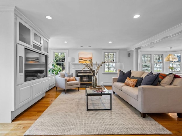 living area with recessed lighting, a baseboard radiator, a glass covered fireplace, and light wood finished floors