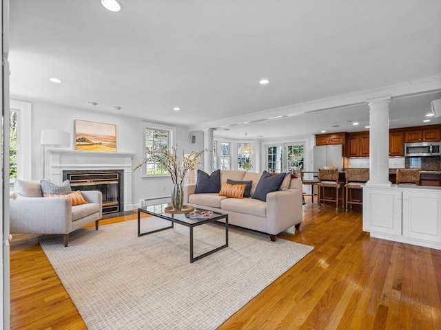 living room featuring recessed lighting, a fireplace with flush hearth, light wood-style flooring, and ornate columns