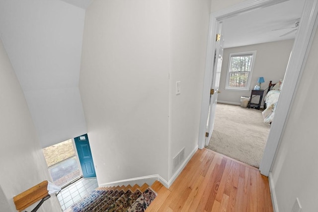 hall featuring light colored carpet, visible vents, light wood finished floors, and baseboards