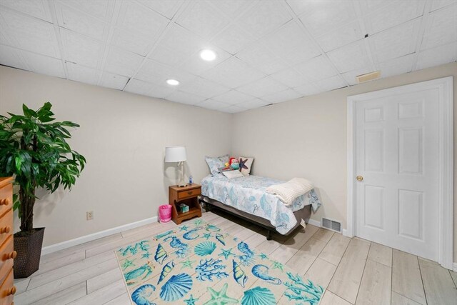 bedroom with a drop ceiling, wood finished floors, visible vents, and baseboards