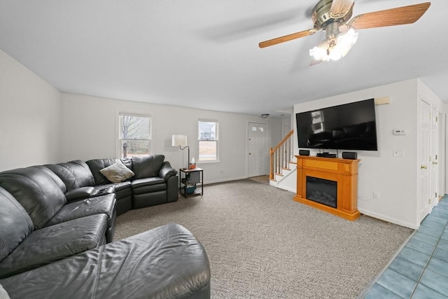 carpeted living area featuring ceiling fan, stairway, a glass covered fireplace, and baseboards