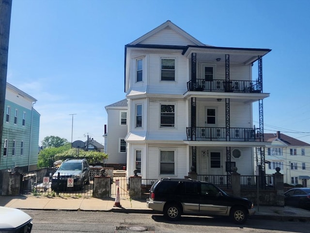 townhome / multi-family property featuring a balcony, a fenced front yard, a gate, and a porch