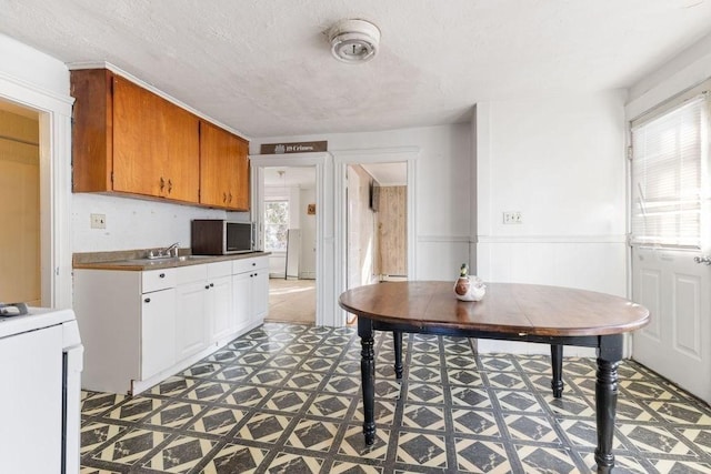 78 Endicott St, Peabody, MA 01960 - kitchen with tile patterned floors, stainless steel microwave, wainscoting, a sink, and brown cabinets