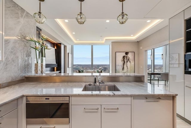 kitchen with sink, white cabinetry, hanging light fixtures, and light stone counters