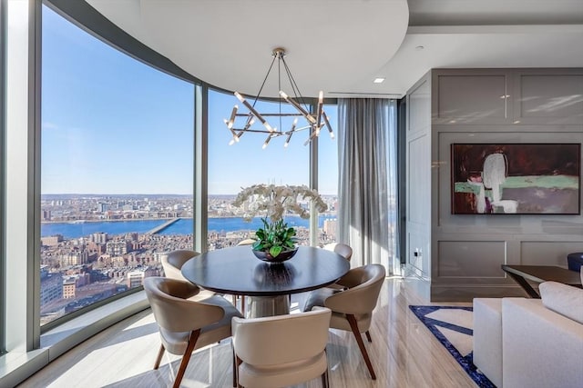 dining area featuring a chandelier, a water view, expansive windows, and light hardwood / wood-style flooring