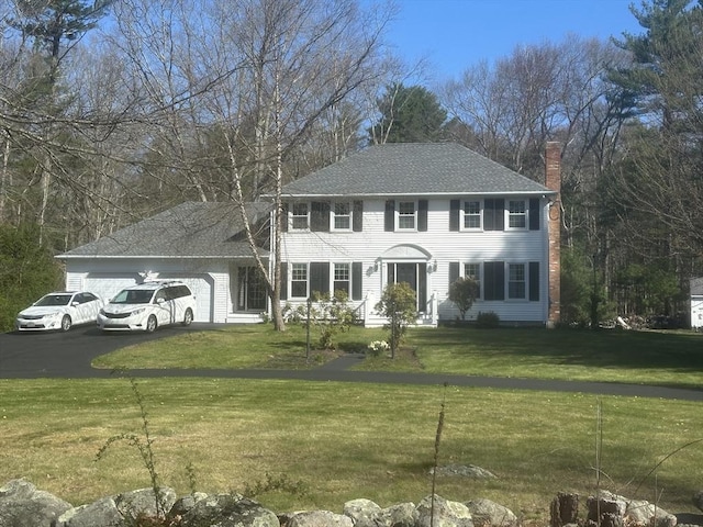 colonial house featuring a chimney, an attached garage, a front yard, and asphalt driveway