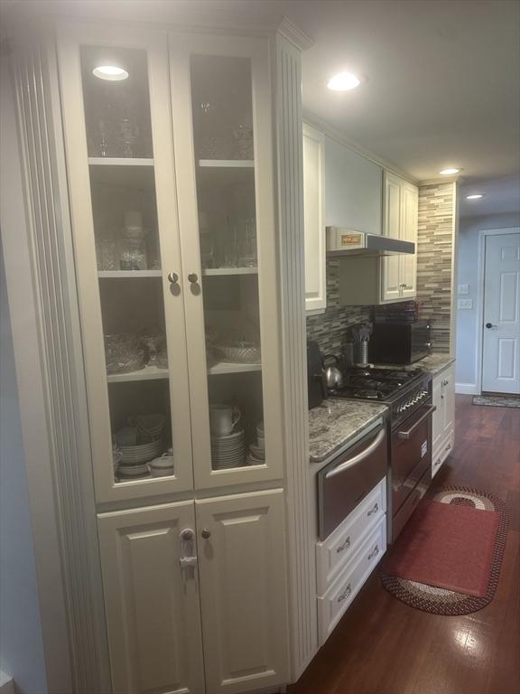 kitchen featuring high end stove, a warming drawer, white cabinetry, dark wood-style floors, and backsplash