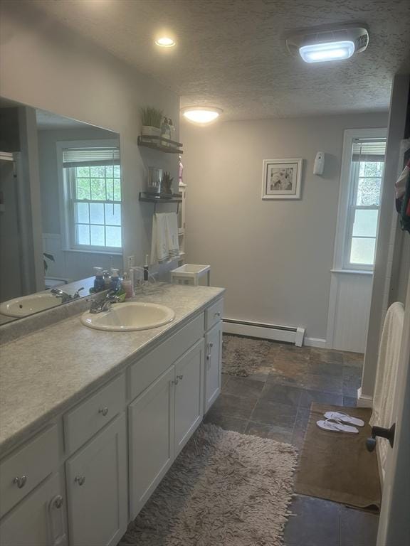 full bath featuring a baseboard radiator, vanity, a textured ceiling, and stone finish floors