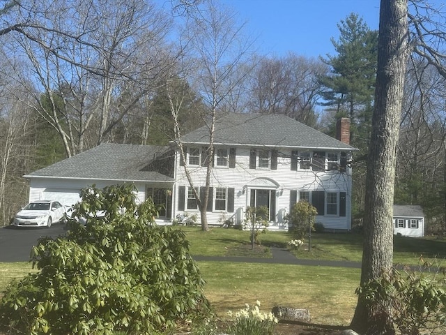 view of front of home featuring a garage, a front lawn, a chimney, and a shingled roof