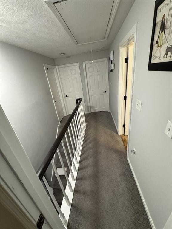 corridor featuring attic access, baseboards, and dark carpet