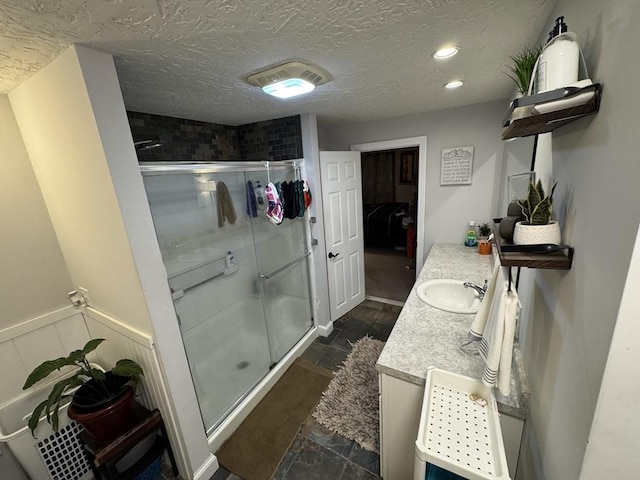 full bath with a shower stall, vanity, stone finish flooring, a textured ceiling, and recessed lighting