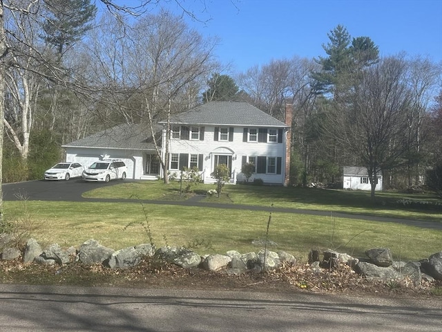colonial house featuring a garage, a chimney, asphalt driveway, and a front lawn