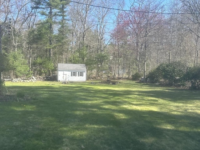 view of grassy yard with an outbuilding, a shed, and a view of trees