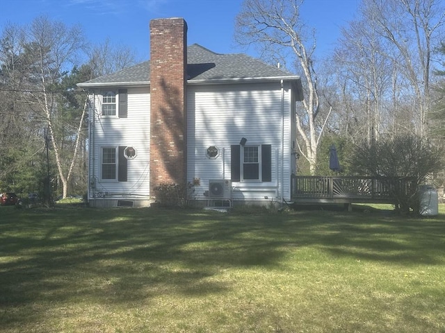 back of house featuring a chimney, a yard, a deck, and roof with shingles