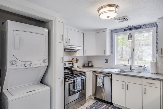 kitchen featuring appliances with stainless steel finishes, stacked washer / dryer, a sink, under cabinet range hood, and white cabinets