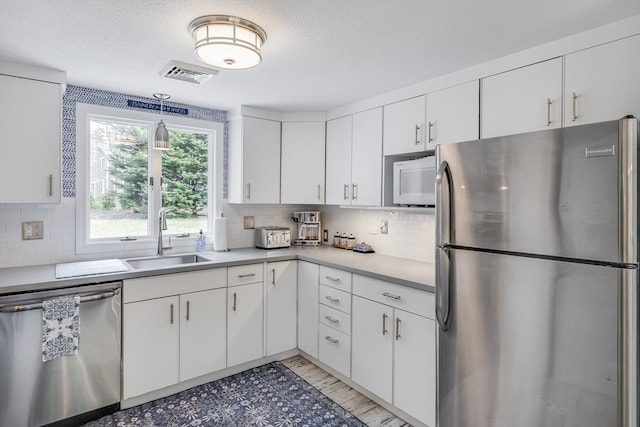 kitchen featuring appliances with stainless steel finishes, a sink, light countertops, tasteful backsplash, and white cabinetry