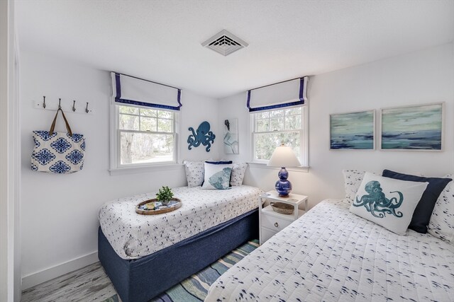bedroom with multiple windows, baseboards, and wood finished floors