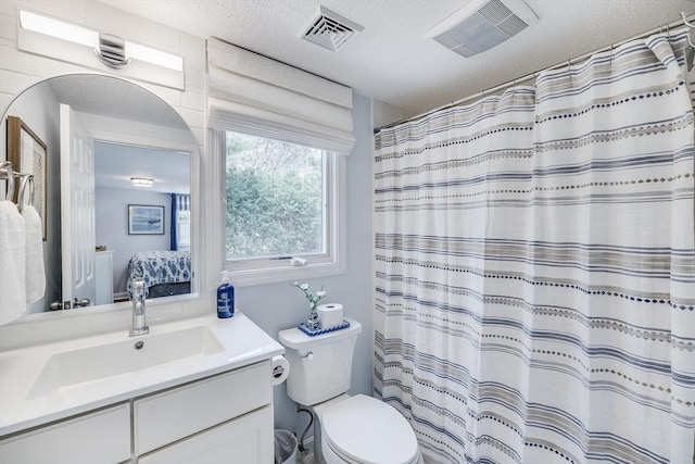 ensuite bathroom featuring a textured ceiling, vanity, toilet, and curtained shower