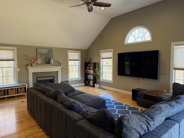 living room featuring high vaulted ceiling, light wood-type flooring, a ceiling fan, a tile fireplace, and baseboards
