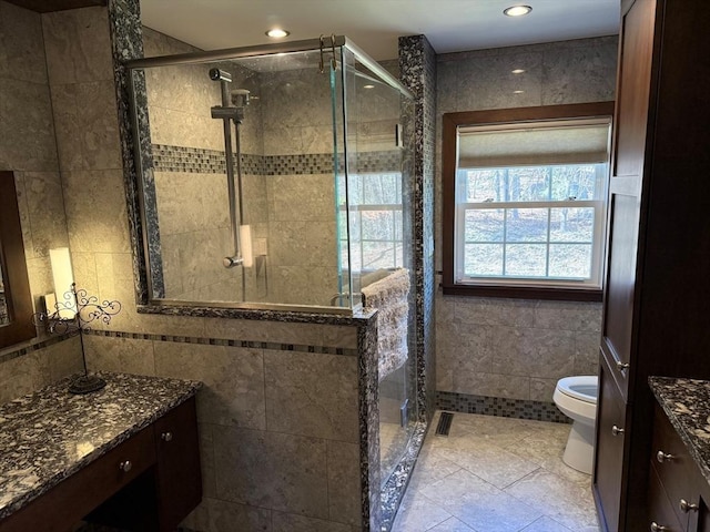 full bathroom featuring a shower stall, vanity, tile walls, and toilet