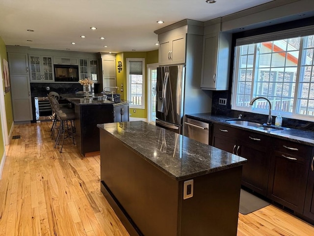 kitchen with dark stone countertops, plenty of natural light, a sink, appliances with stainless steel finishes, and a kitchen island