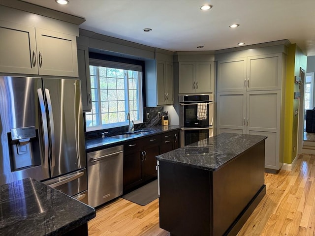 kitchen featuring light wood-style floors, dark stone counters, a kitchen island, appliances with stainless steel finishes, and a sink