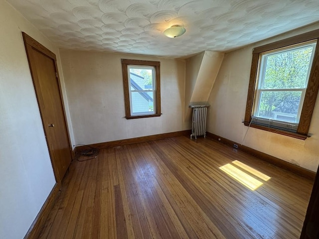 additional living space featuring baseboards, radiator, and hardwood / wood-style floors