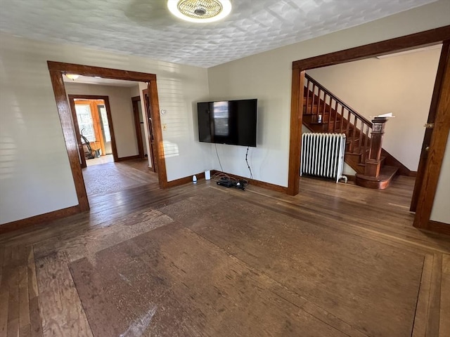 unfurnished living room with baseboards, radiator heating unit, stairway, and wood finished floors