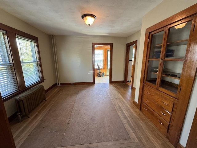 unfurnished room with baseboards, a healthy amount of sunlight, radiator heating unit, and wood finished floors