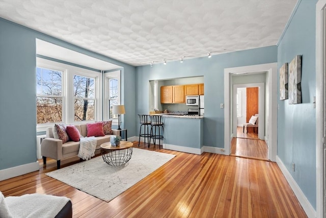 living room with light wood-type flooring, baseboards, track lighting, and radiator heating unit