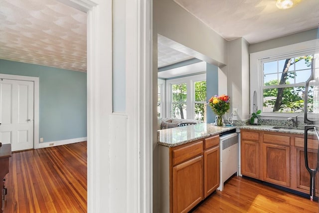 kitchen with plenty of natural light, brown cabinets, wood finished floors, and light stone countertops