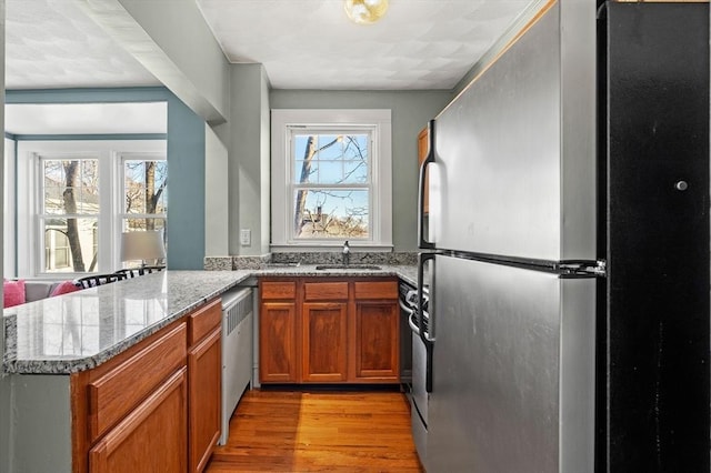 kitchen with a peninsula, light wood-style flooring, freestanding refrigerator, a sink, and brown cabinets