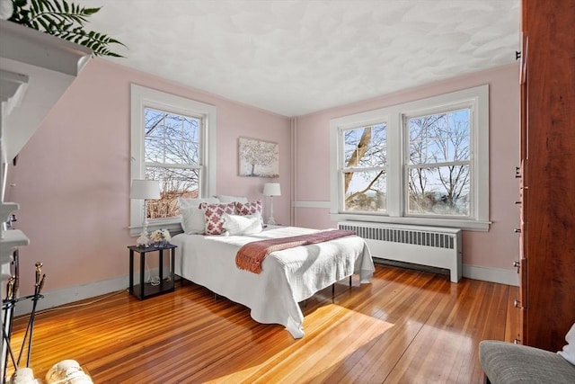 bedroom featuring hardwood / wood-style flooring, radiator, and baseboards