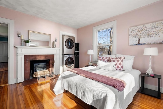 bedroom with baseboards, stacked washer and dryer, a brick fireplace, and hardwood / wood-style floors