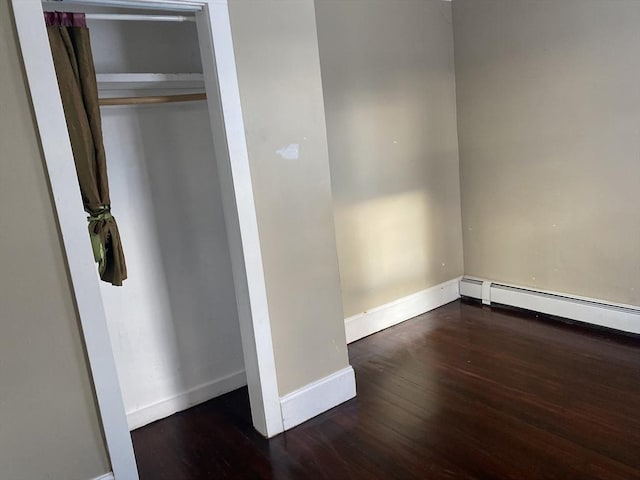 unfurnished bedroom with dark wood-type flooring, baseboard heating, and a closet