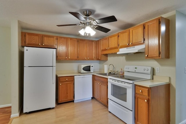 kitchen featuring under cabinet range hood, light countertops, light wood-style flooring, white appliances, and a sink