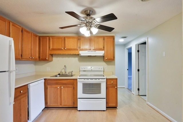 kitchen with white appliances, a sink, light countertops, under cabinet range hood, and light wood-type flooring