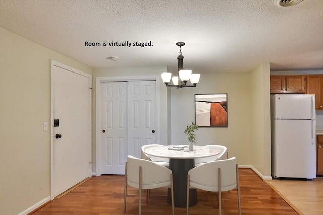 dining area featuring light wood finished floors, a textured ceiling, baseboards, and an inviting chandelier