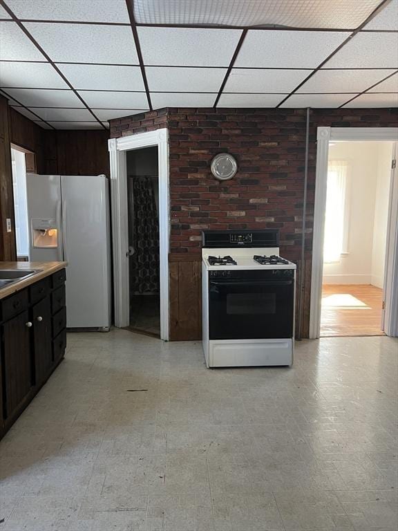 kitchen with a paneled ceiling, light floors, white refrigerator with ice dispenser, and range with gas cooktop