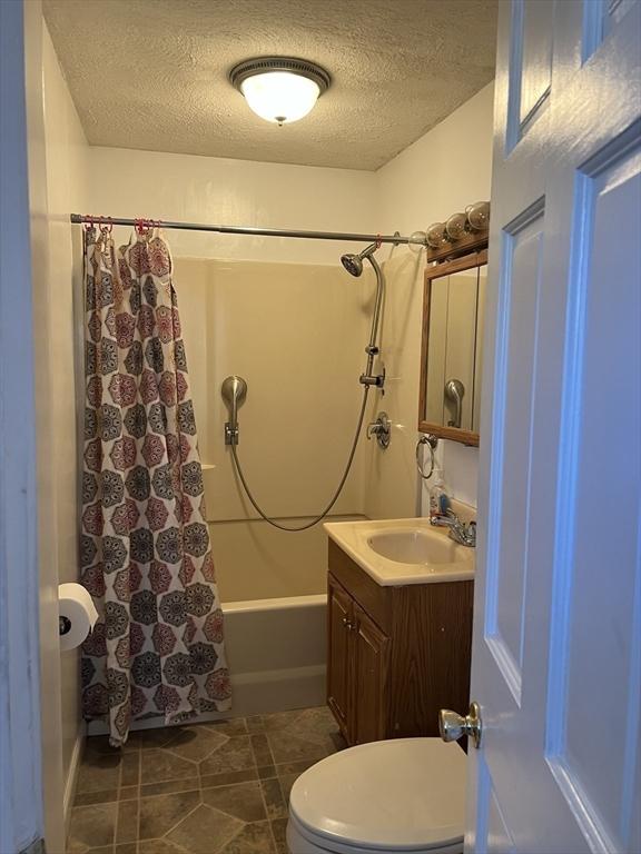 bathroom with toilet, shower / bath combo with shower curtain, a textured ceiling, vanity, and tile patterned flooring