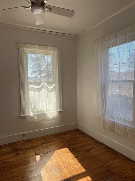 spare room with ornamental molding, wood-type flooring, a ceiling fan, and baseboards