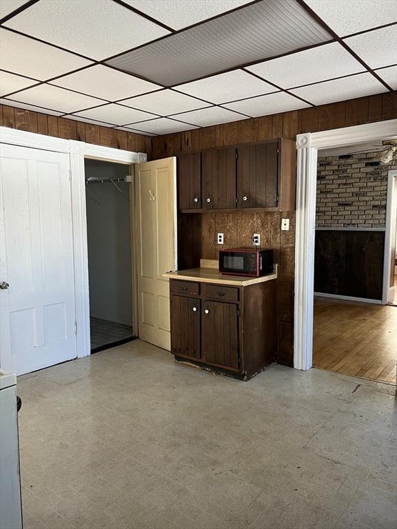 kitchen with light floors, black microwave, dark brown cabinets, and wood walls