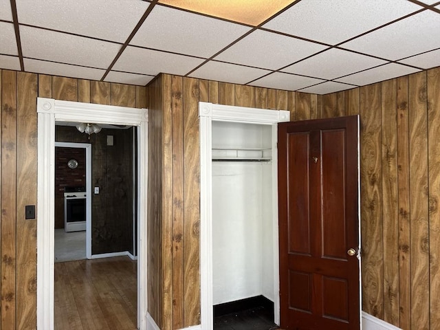 unfurnished bedroom featuring a closet, wood walls, dark wood finished floors, and a paneled ceiling