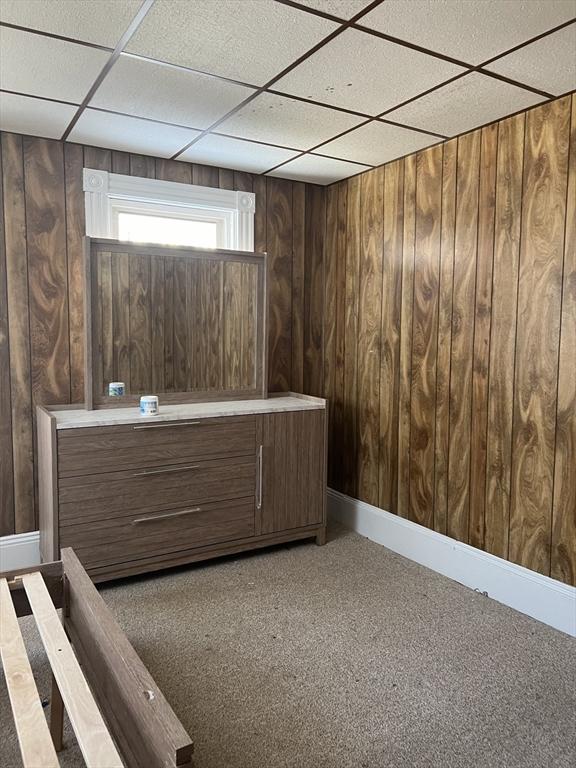 interior space featuring a paneled ceiling, wooden walls, and baseboards