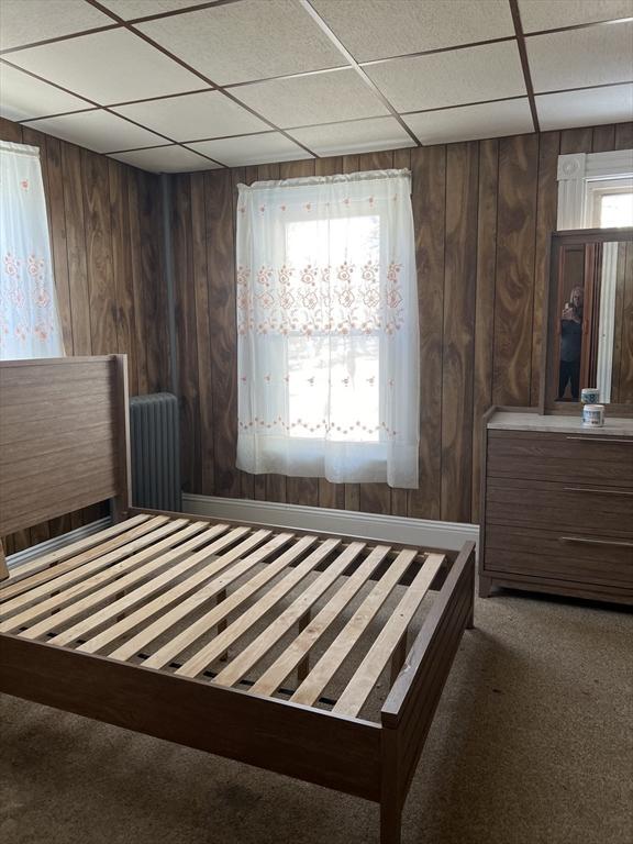 unfurnished bedroom with multiple windows, wood walls, carpet, and a paneled ceiling